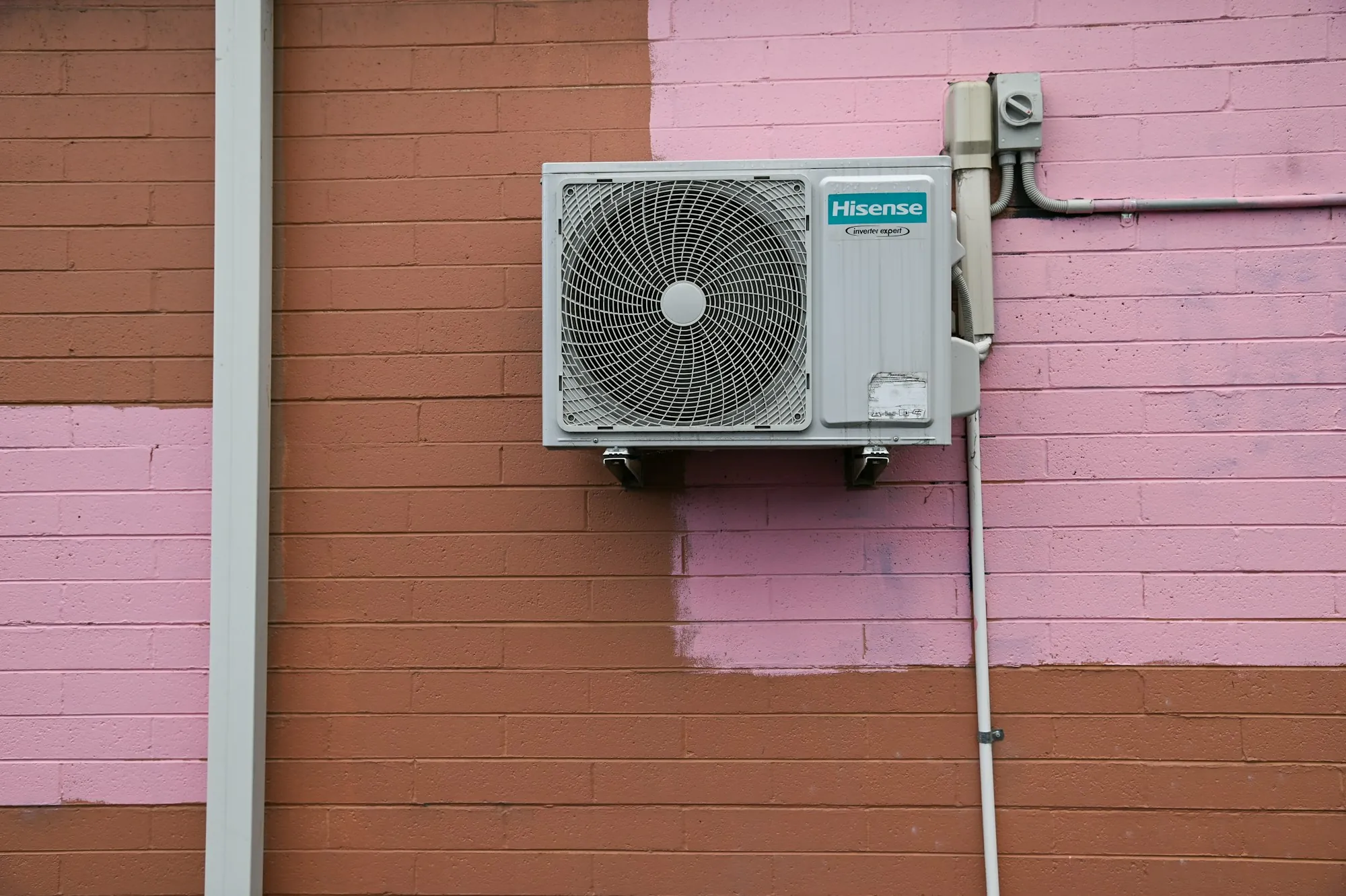 Outdoor AC condenser mounted on a red brick wall